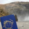 Travelfolio mit goldener Weltkartenverzierung wird vor einem Wasserfall in einer natürlichen Landschaft gehalten